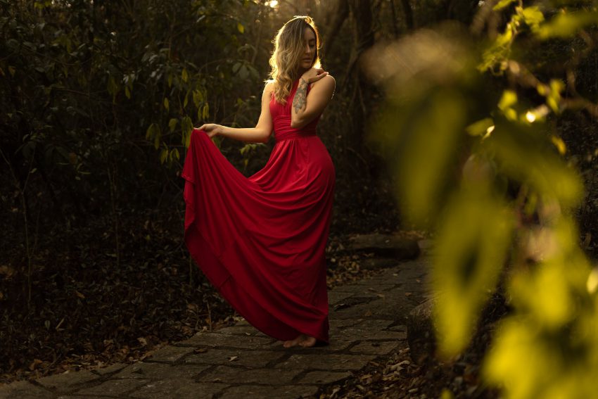 kobieta w czerwonej sukience między zielonymi drzewami