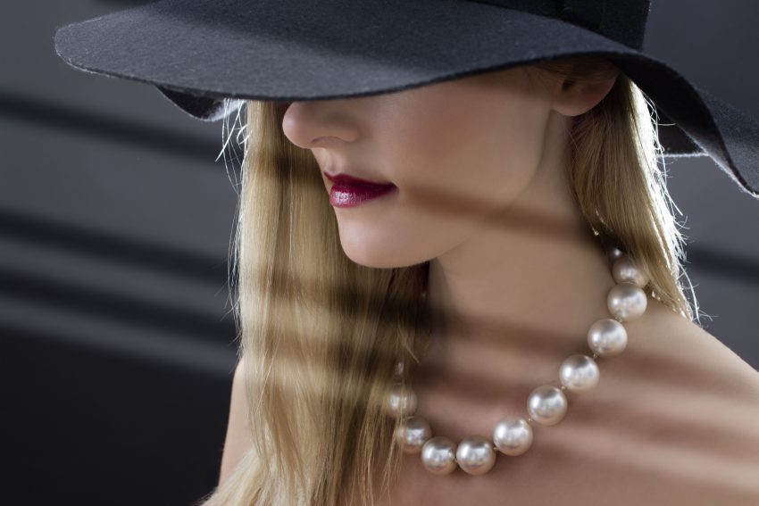 kobieta w czarnym kapeluszu z perłami na szyi